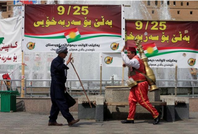 رجلان يسيران بالقرب من لافتات تؤيد استفتاء كردستان